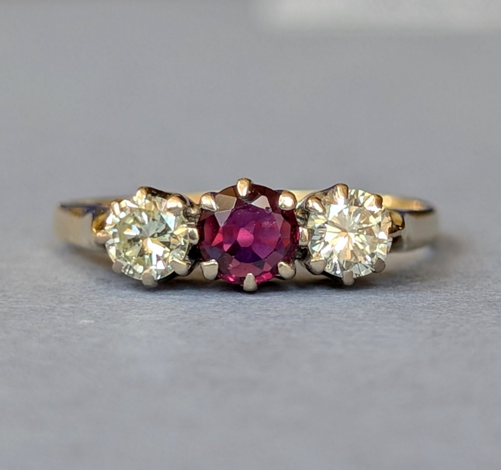 An 18ct gold trilogy ring featuring a round central red ruby flanked by two diamonds in claw settings.
