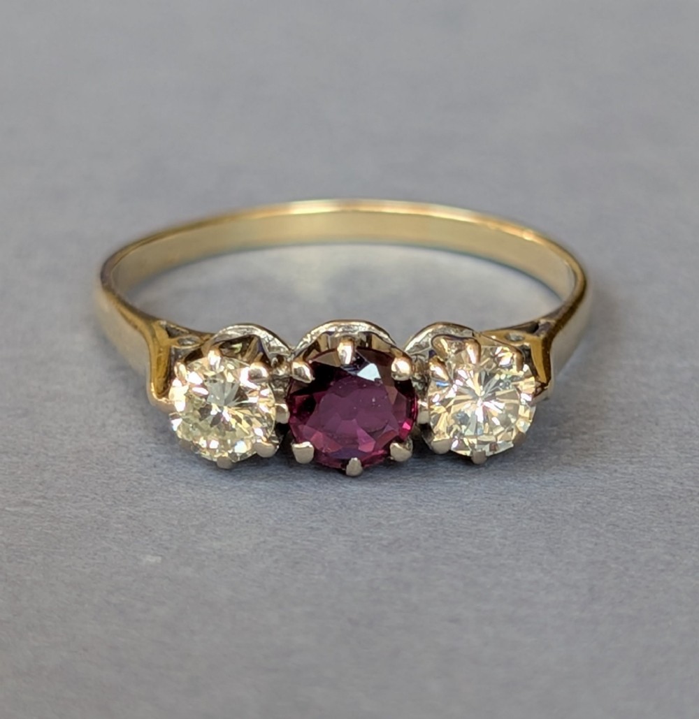 An 18ct gold trilogy ring featuring a round central red ruby flanked by two diamonds in claw settings. View III