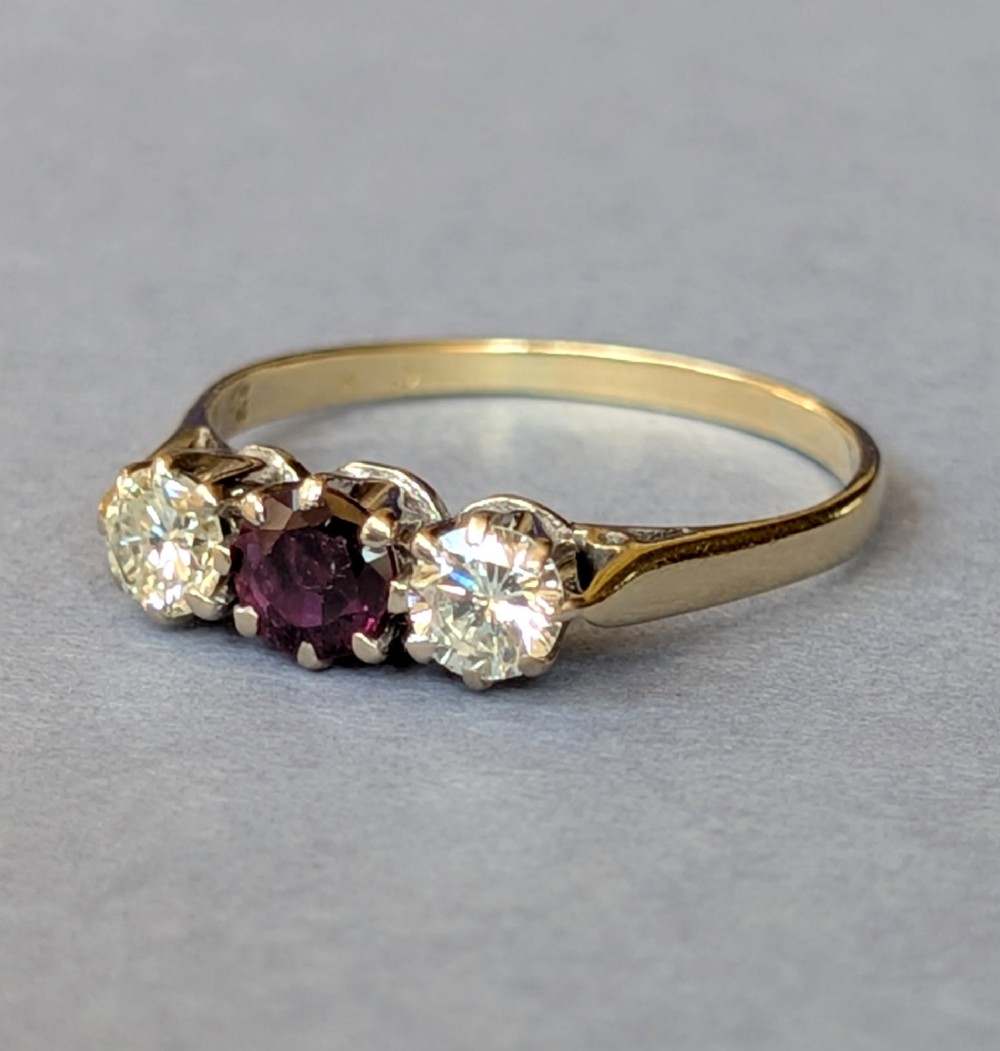 An 18ct gold trilogy ring featuring a round central red ruby flanked by two diamonds in claw settings. View IV