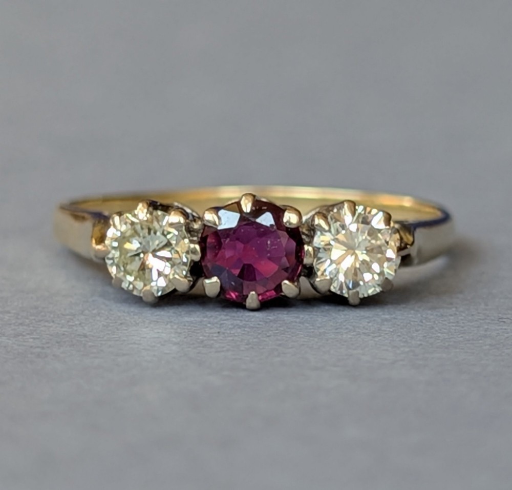 An 18ct gold trilogy ring featuring a round central red ruby flanked by two diamonds in claw settings. View V