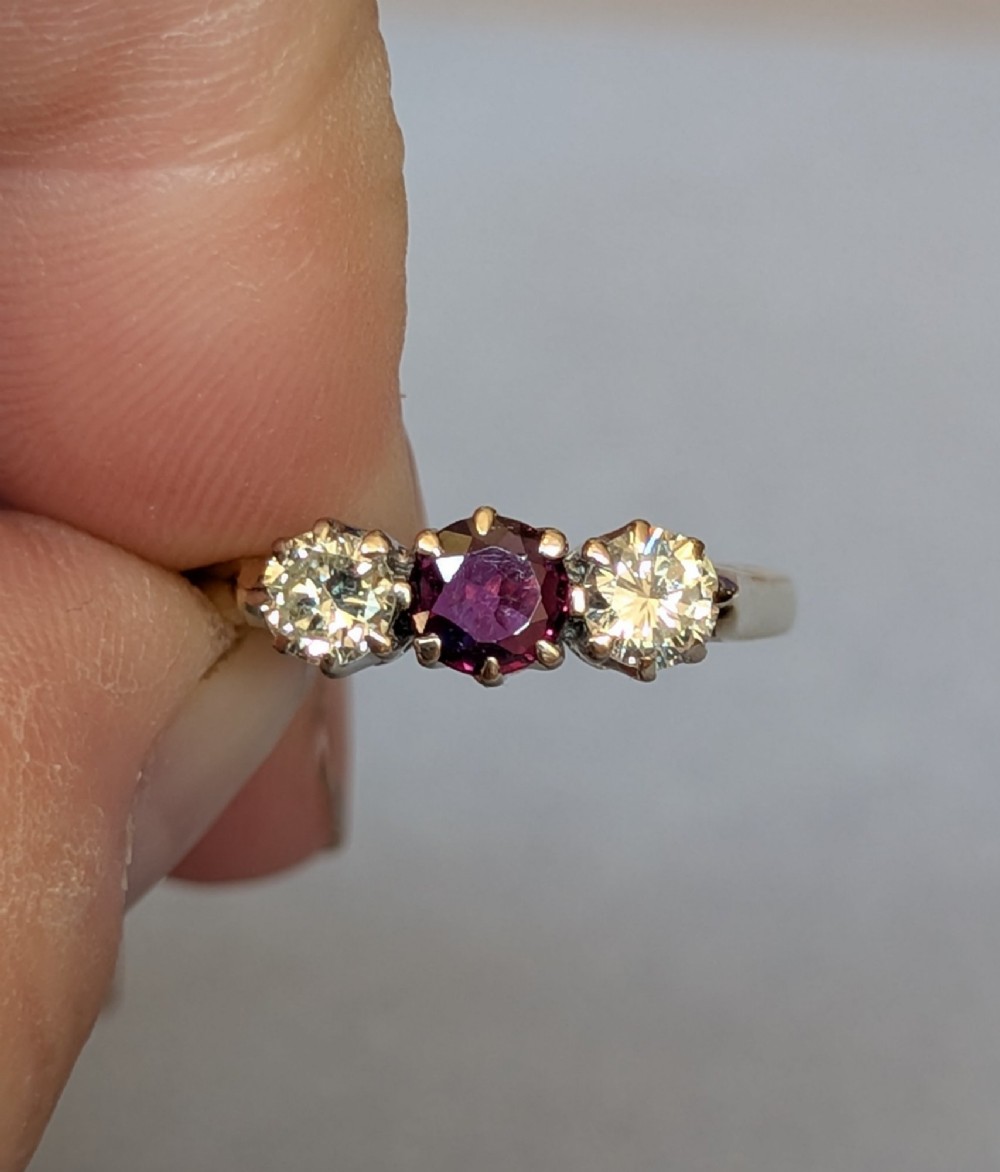 An 18ct gold trilogy ring featuring a round central red ruby flanked by two diamonds in claw settings. View VII