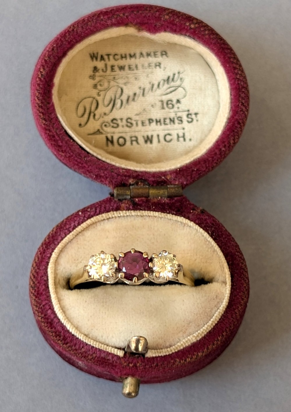 An 18ct gold trilogy ring featuring a round central red ruby flanked by two diamonds in claw settings. View VIII