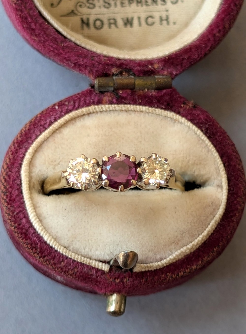 An 18ct gold trilogy ring featuring a round central red ruby flanked by two diamonds in claw settings. View IX