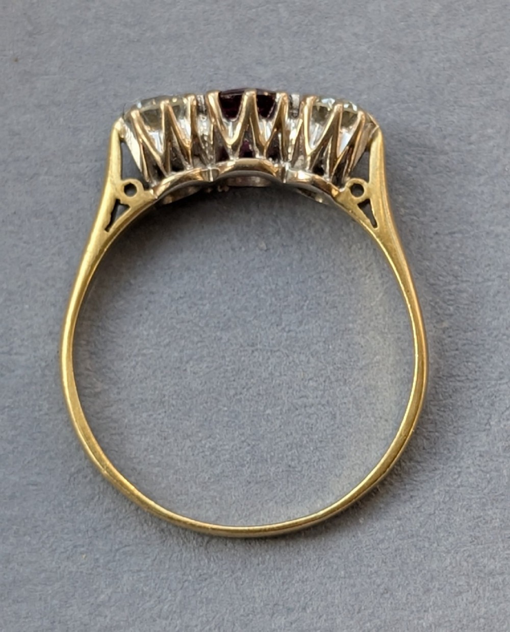 An 18ct gold trilogy ring featuring a round central red ruby flanked by two diamonds in claw settings. View X