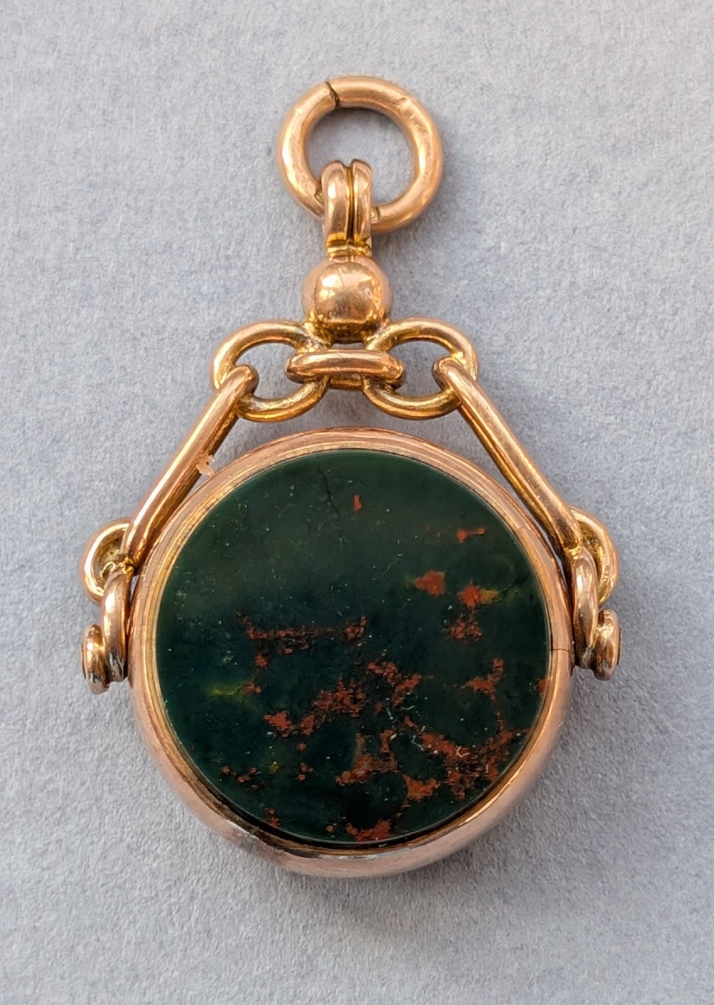 An Edwardian 9ct gold spinning fob pendant set with a polished circular dark green bloodstone gemstone with red flecks.