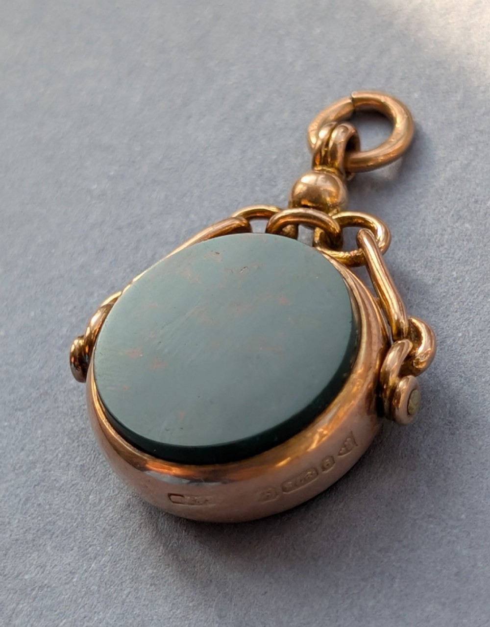 An Edwardian 9ct gold spinning fob pendant set with a polished circular dark green bloodstone gemstone with red flecks. View VI