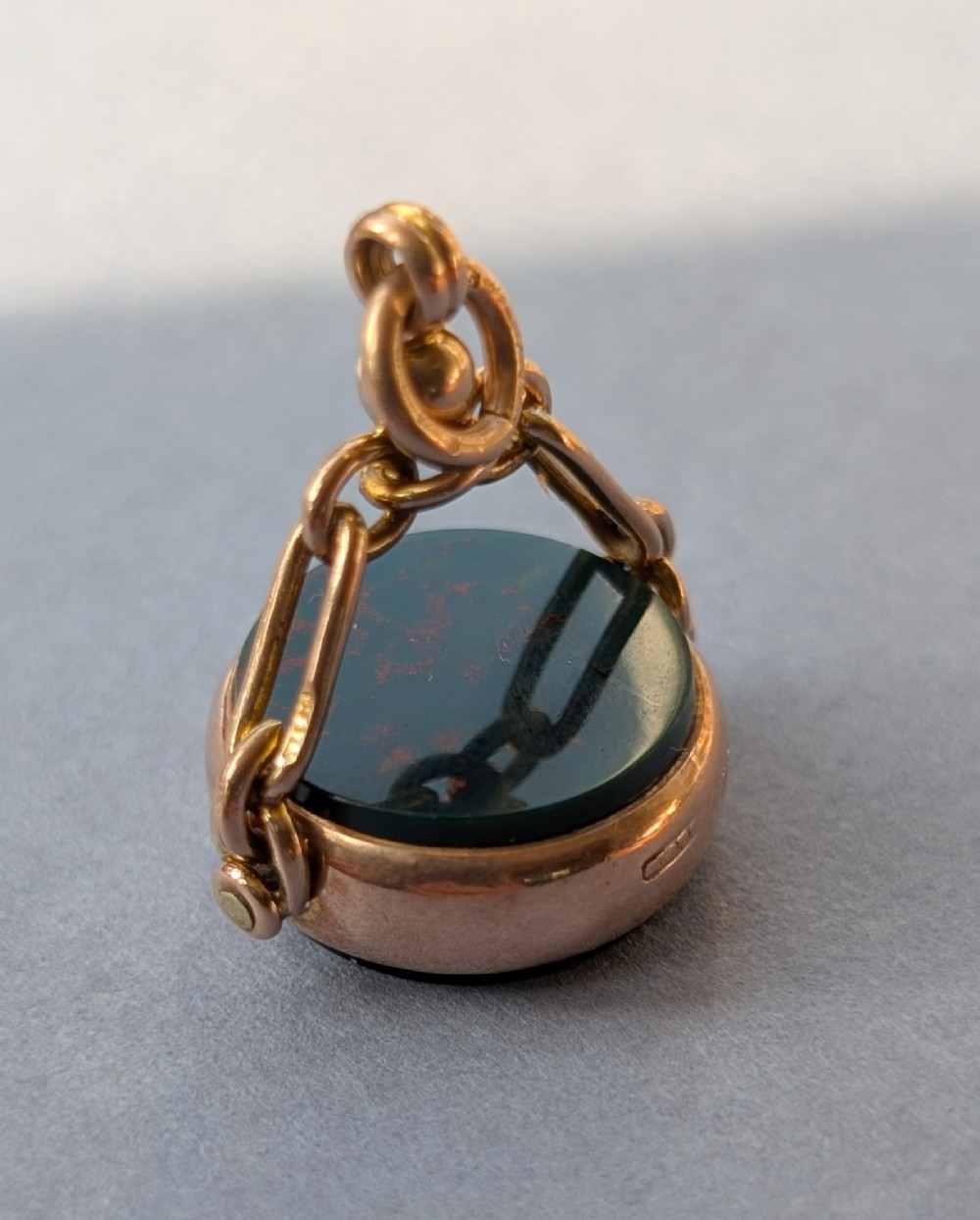An Edwardian 9ct gold spinning fob pendant set with a polished circular dark green bloodstone gemstone with red flecks. View IX