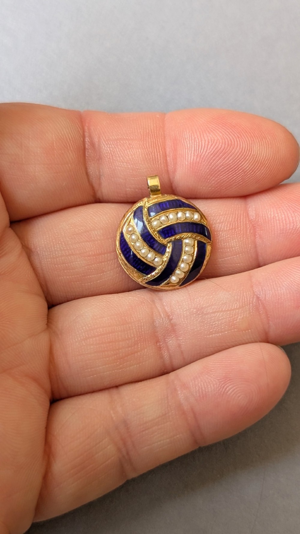 A circular Victorian gold pendant featuring spiralling bands of cobalt blue enamel and set split pearls. View IV