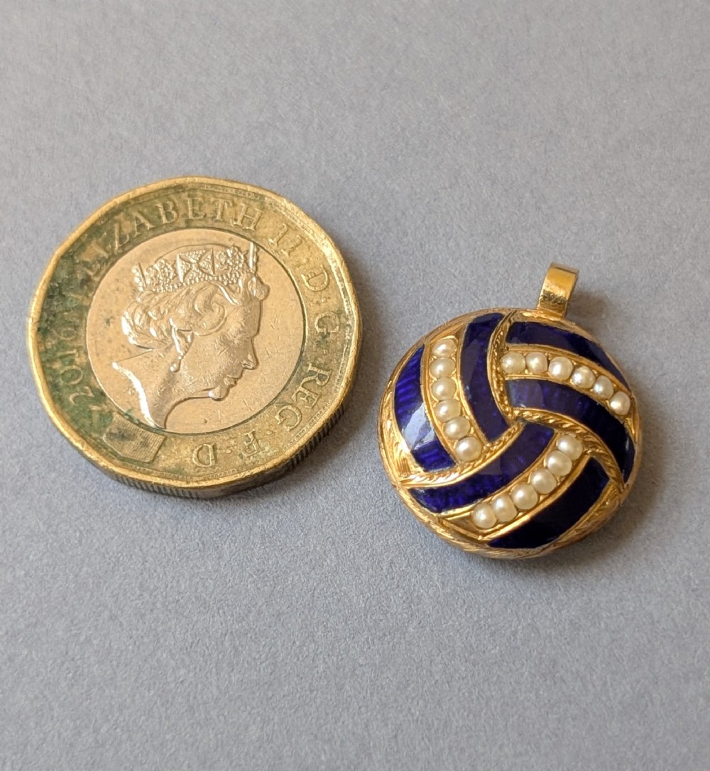 A circular Victorian gold pendant featuring spiralling bands of cobalt blue enamel and set split pearls. View V
