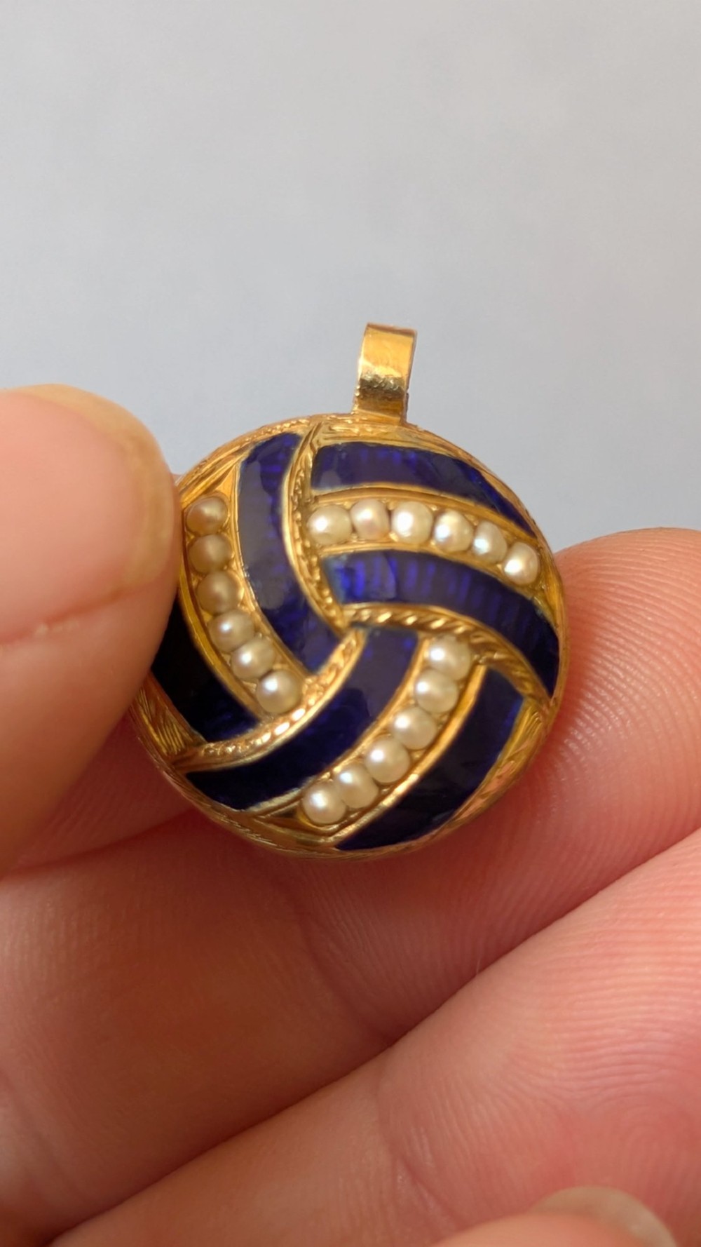 A circular Victorian gold pendant featuring spiralling bands of cobalt blue enamel and set split pearls. View X