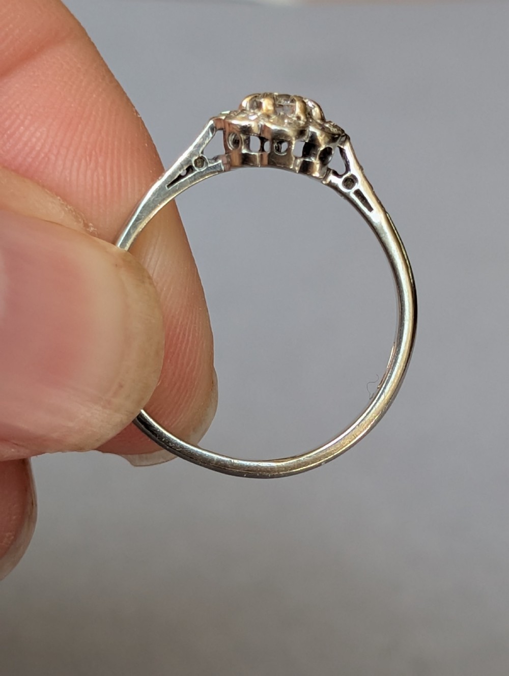 An Art Deco diamond daisy cluster ring with a circular central diamond surrounded by eight smaller diamonds set on a polished band with detailed shoulders. View VII