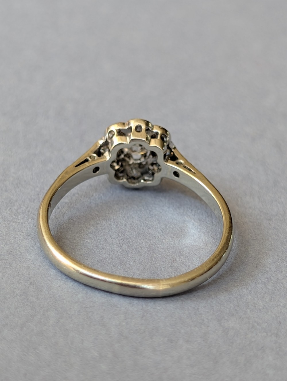 An Art Deco diamond daisy cluster ring with a circular central diamond surrounded by eight smaller diamonds set on a polished band with detailed shoulders. View VIII
