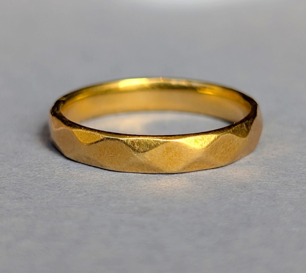 A vintage 18ct yellow gold wedding band featuring a faceted geometric pattern around the exterior surface.