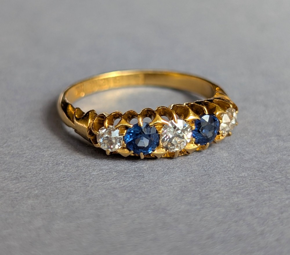 An Edwardian 18ct yellow gold five-stone ring featuring alternating blue sapphires and old cut diamonds set within a carved scroll head. View III