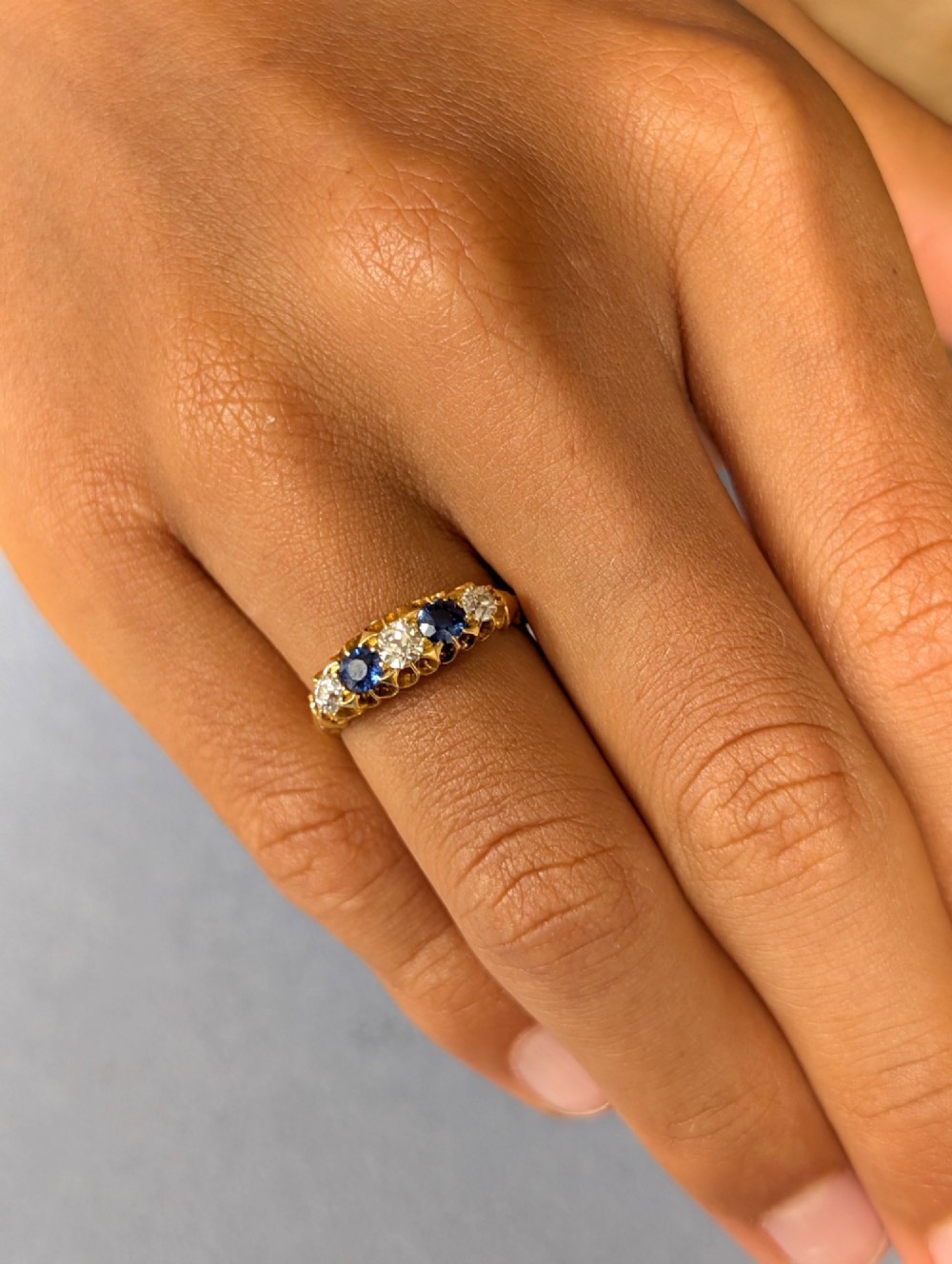 An Edwardian 18ct yellow gold five-stone ring featuring alternating blue sapphires and old cut diamonds set within a carved scroll head. View VI