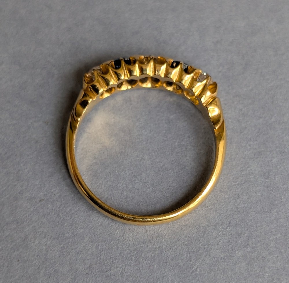 An Edwardian 18ct yellow gold five-stone ring featuring alternating blue sapphires and old cut diamonds set within a carved scroll head. View VIII