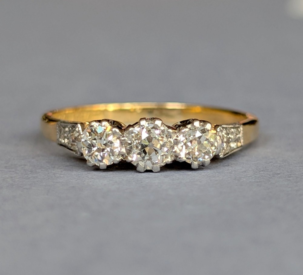 An 18ct yellow gold Art Deco ring featuring three round diamonds set horizontally with platinum-mounted diamond accents on the shoulders.