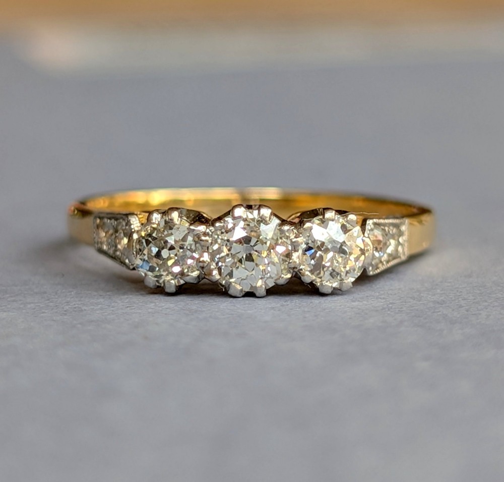 An 18ct yellow gold Art Deco ring featuring three round diamonds set horizontally with platinum-mounted diamond accents on the shoulders. View II