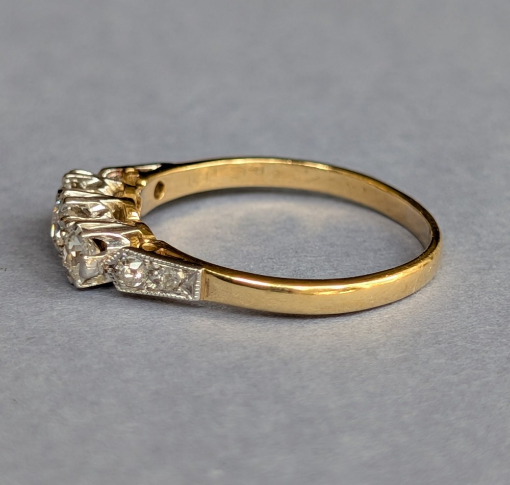 An 18ct yellow gold Art Deco ring featuring three round diamonds set horizontally with platinum-mounted diamond accents on the shoulders. View III