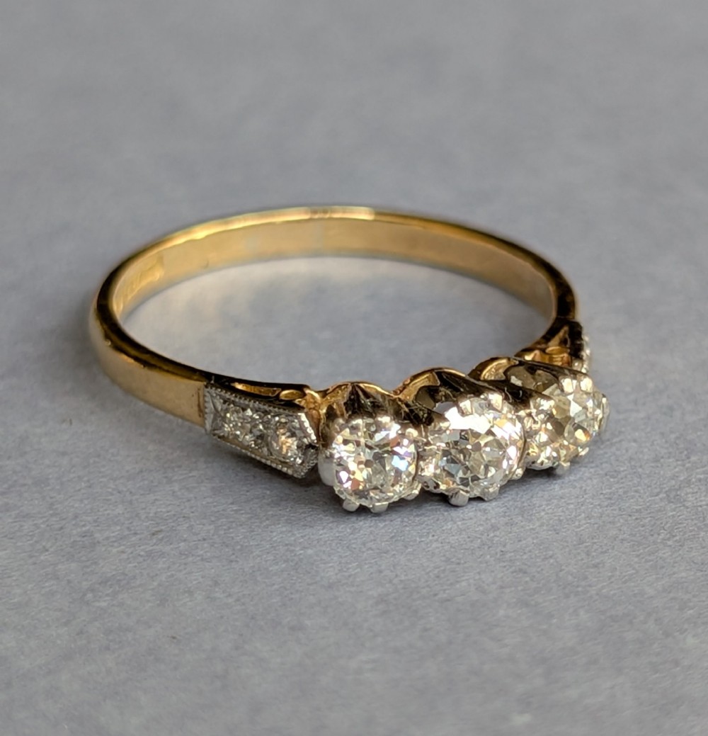An 18ct yellow gold Art Deco ring featuring three round diamonds set horizontally with platinum-mounted diamond accents on the shoulders. View IV