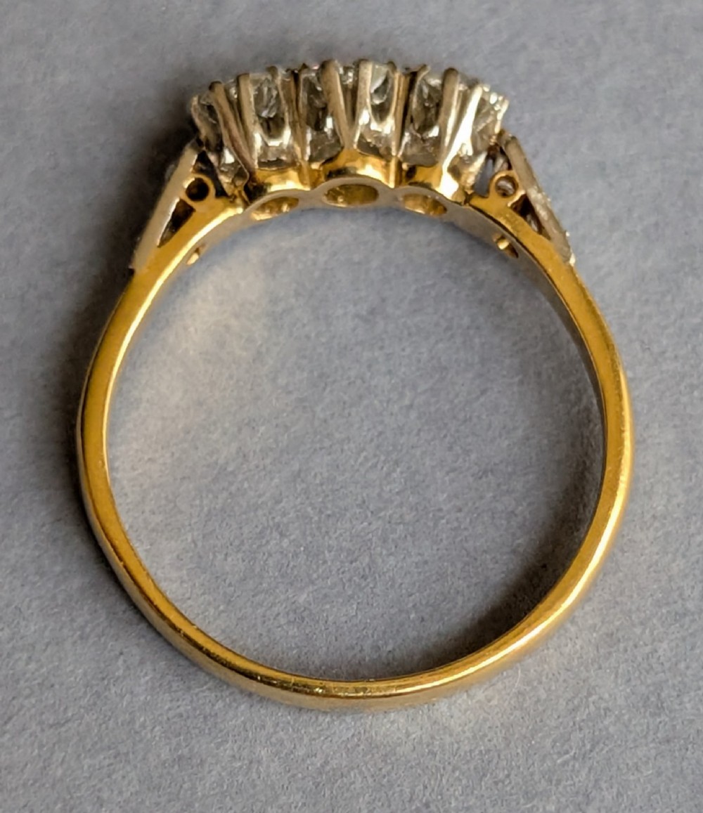 An 18ct yellow gold Art Deco ring featuring three round diamonds set horizontally with platinum-mounted diamond accents on the shoulders. View V