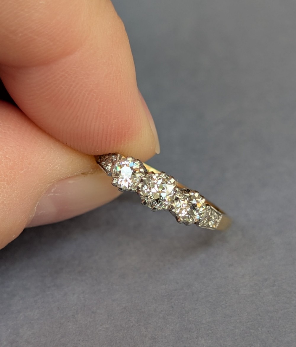 An 18ct yellow gold Art Deco ring featuring three round diamonds set horizontally with platinum-mounted diamond accents on the shoulders. View VI
