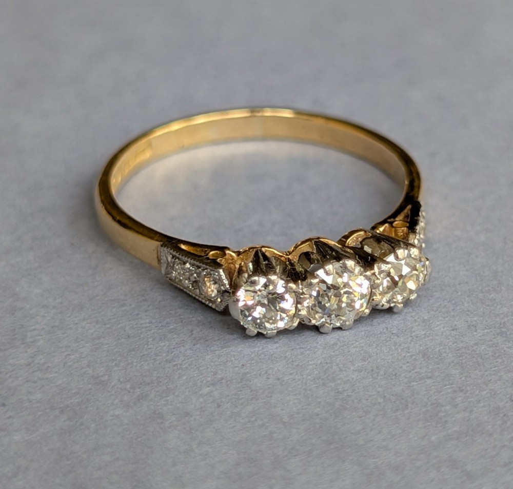 An 18ct yellow gold Art Deco ring featuring three round diamonds set horizontally with platinum-mounted diamond accents on the shoulders. View VII
