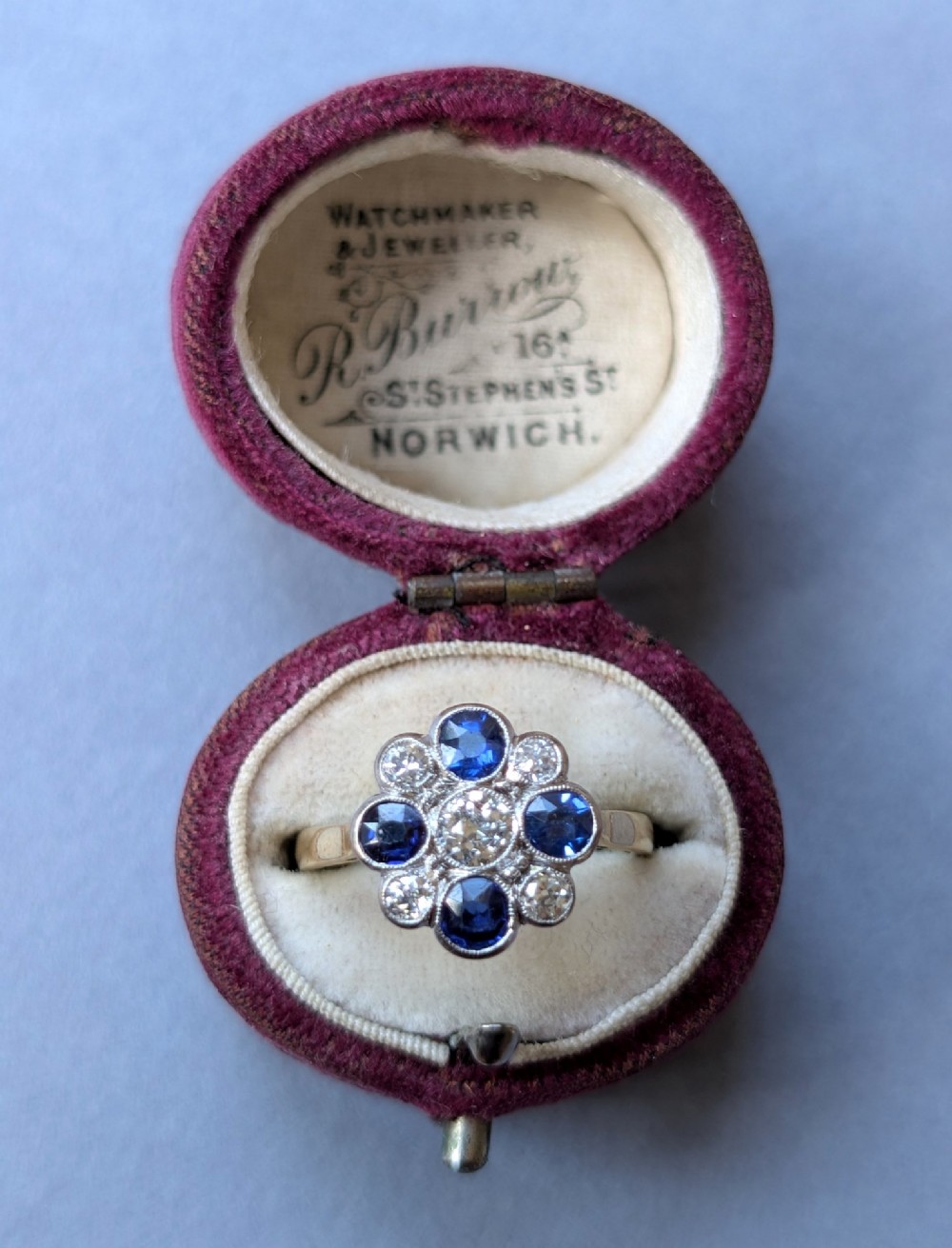 An Art Deco cluster ring featuring a central round diamond surrounded by alternating blue sapphires and smaller diamonds in a flower formation set on a gold band. View XI