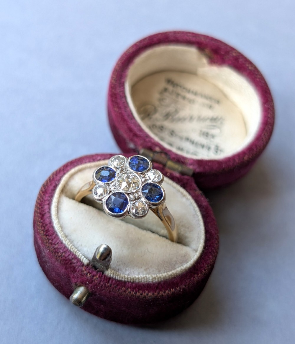 An Art Deco cluster ring featuring a central round diamond surrounded by alternating blue sapphires and smaller diamonds in a flower formation set on a gold band. View XIII
