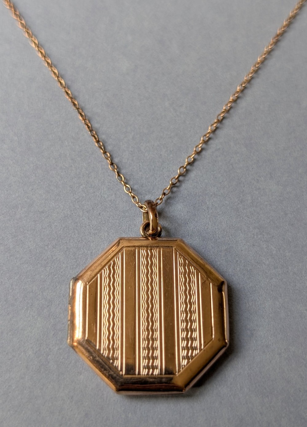 An octagonal 9ct rose gold locket featuring engine-turned geometric engraving suspended from a fine gold chain.