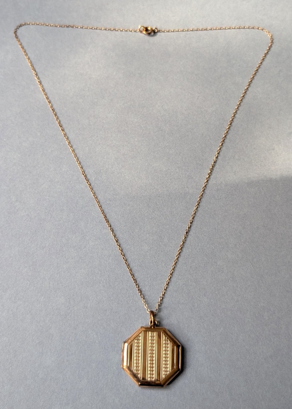 An octagonal 9ct rose gold locket featuring engine-turned geometric engraving suspended from a fine gold chain. View IV