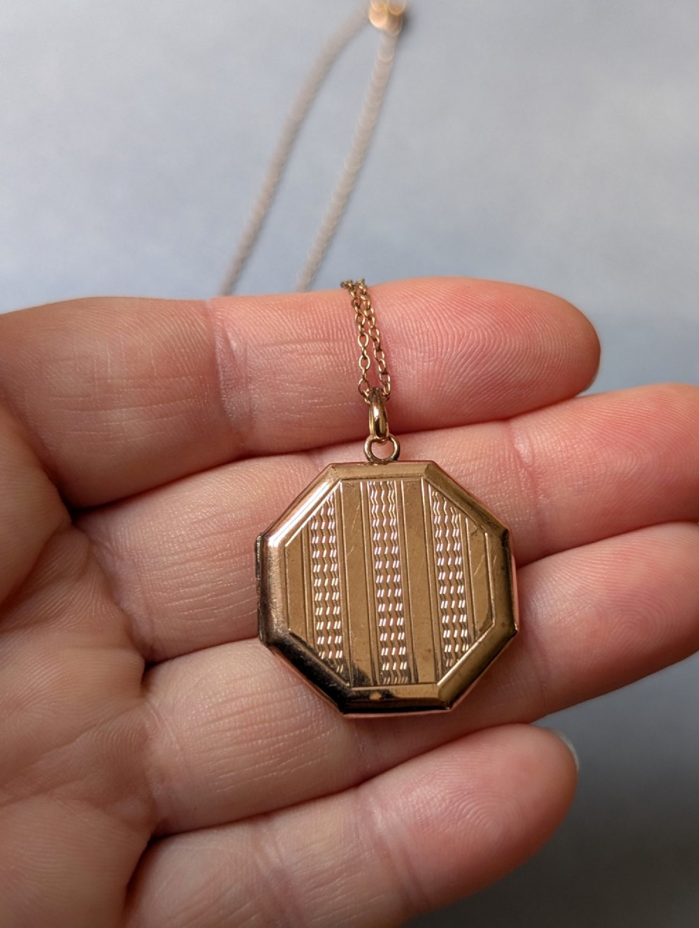 An octagonal 9ct rose gold locket featuring engine-turned geometric engraving suspended from a fine gold chain. View VI