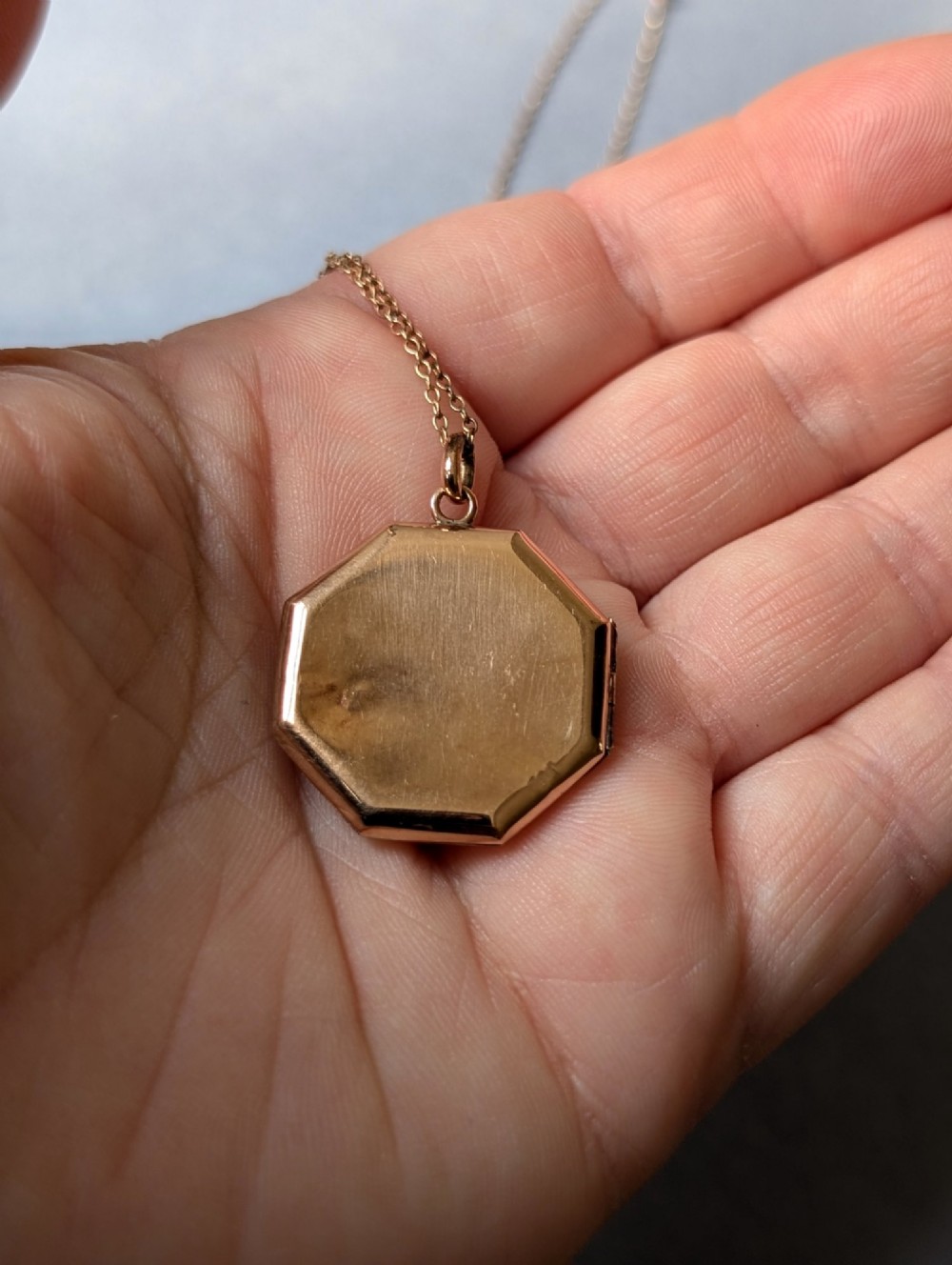 An octagonal 9ct rose gold locket featuring engine-turned geometric engraving suspended from a fine gold chain. View VII