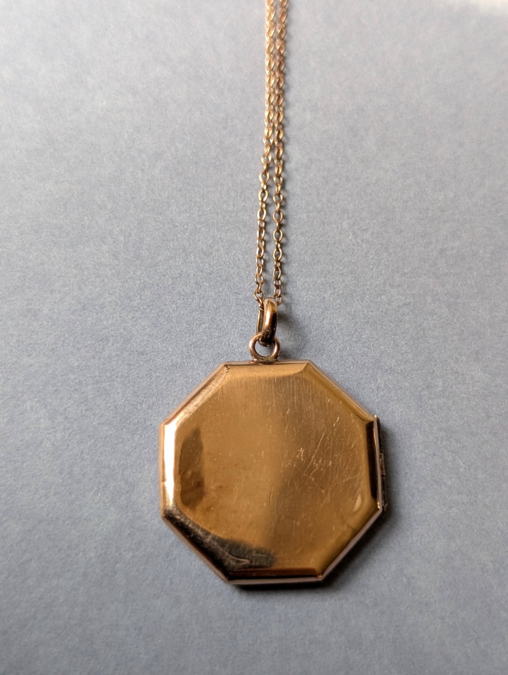 An octagonal 9ct rose gold locket featuring engine-turned geometric engraving suspended from a fine gold chain. View VIII