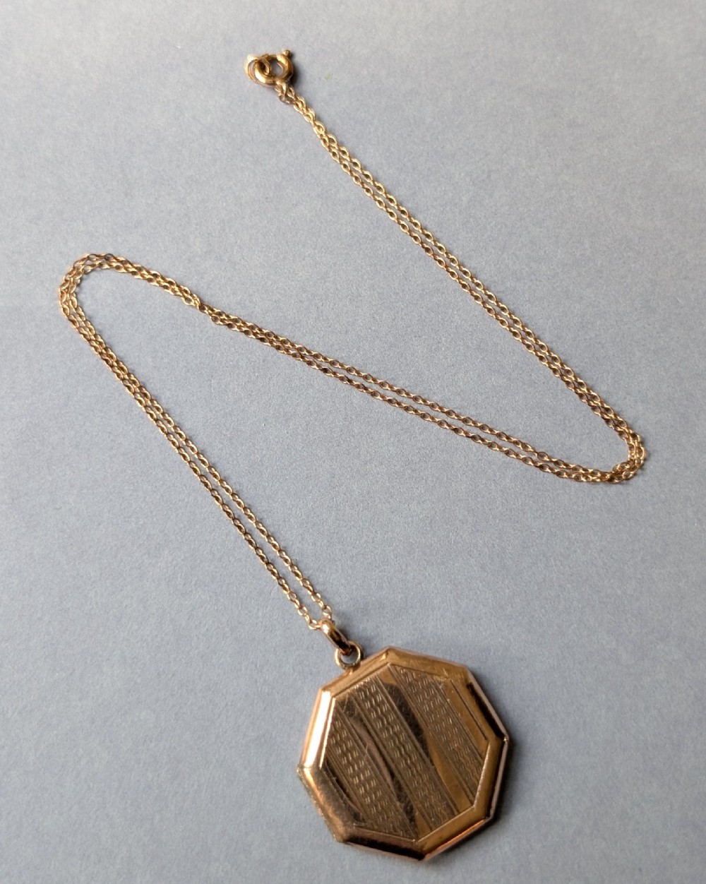 An octagonal 9ct rose gold locket featuring engine-turned geometric engraving suspended from a fine gold chain. View IX