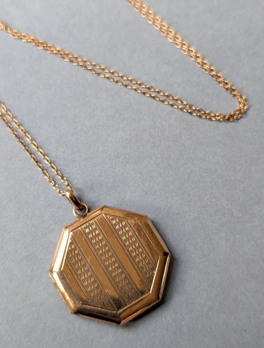 An octagonal 9ct rose gold locket featuring engine-turned geometric engraving suspended from a fine gold chain. View X