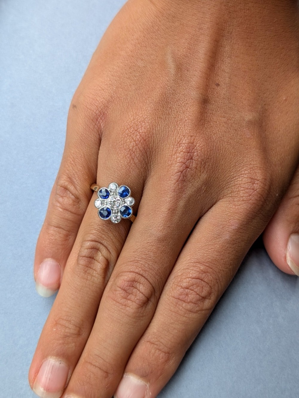An Art Deco cluster ring featuring a central round diamond surrounded by alternating blue sapphires and smaller diamonds in a flower formation set on a gold band. View XIII