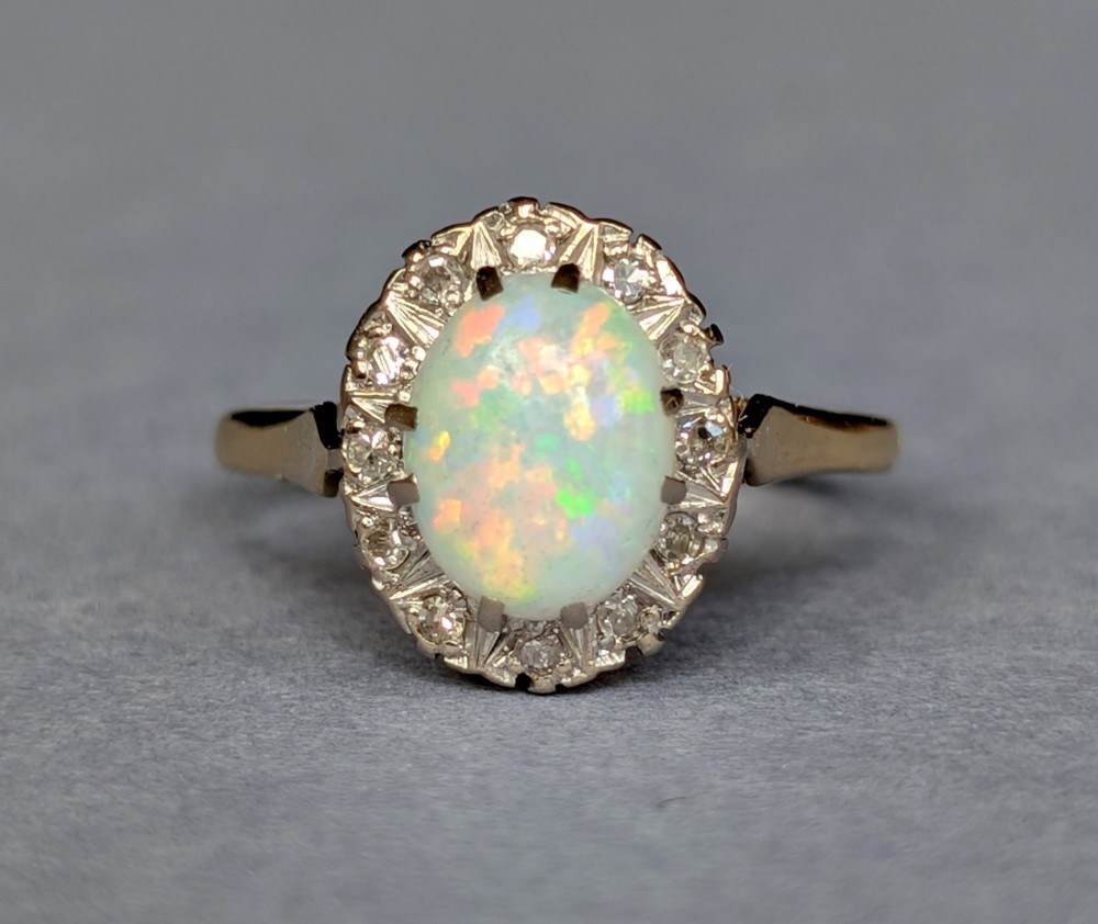 A mid-century 18ct gold ring featuring an oval cabochon opal framed by a halo cluster of small diamonds.