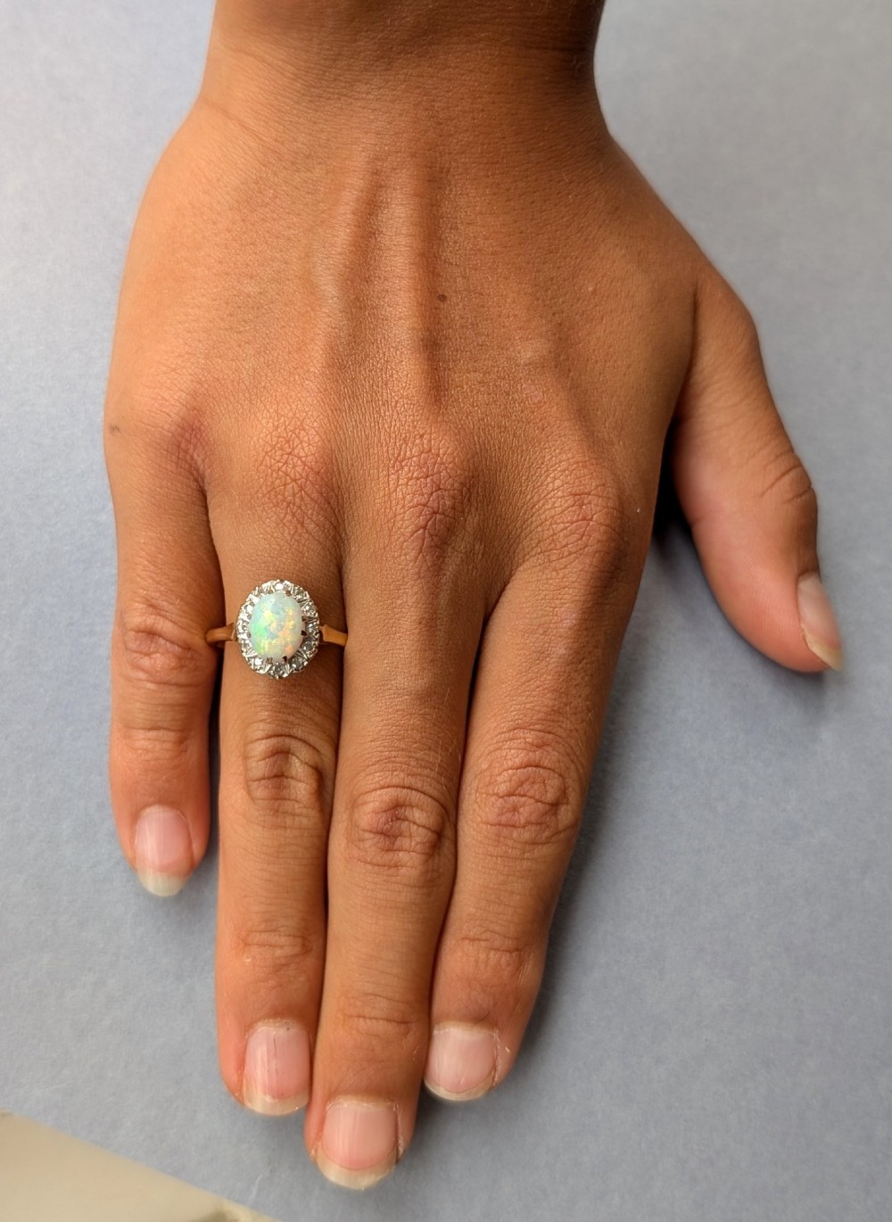 A mid-century 18ct gold ring featuring an oval cabochon opal framed by a halo cluster of small diamonds. View II