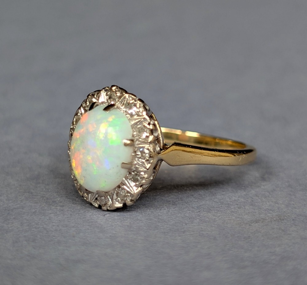 A mid-century 18ct gold ring featuring an oval cabochon opal framed by a halo cluster of small diamonds. View III