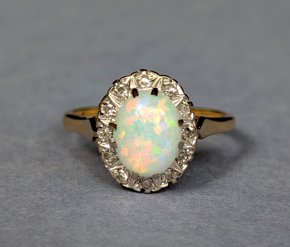 A mid-century 18ct gold ring featuring an oval cabochon opal framed by a halo cluster of small diamonds. View IV