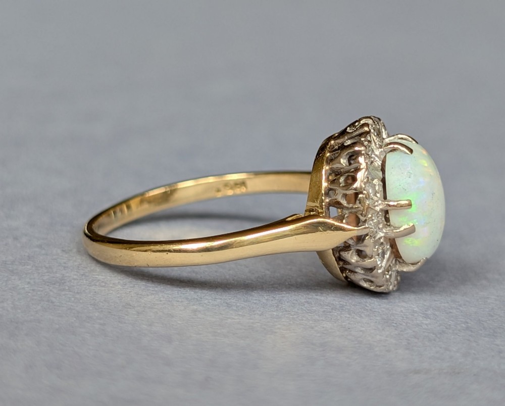 A mid-century 18ct gold ring featuring an oval cabochon opal framed by a halo cluster of small diamonds. View VI