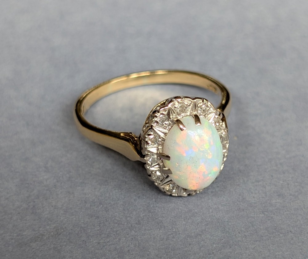 A mid-century 18ct gold ring featuring an oval cabochon opal framed by a halo cluster of small diamonds. View VII