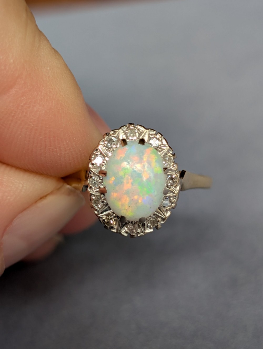 A mid-century 18ct gold ring featuring an oval cabochon opal framed by a halo cluster of small diamonds. View VIII