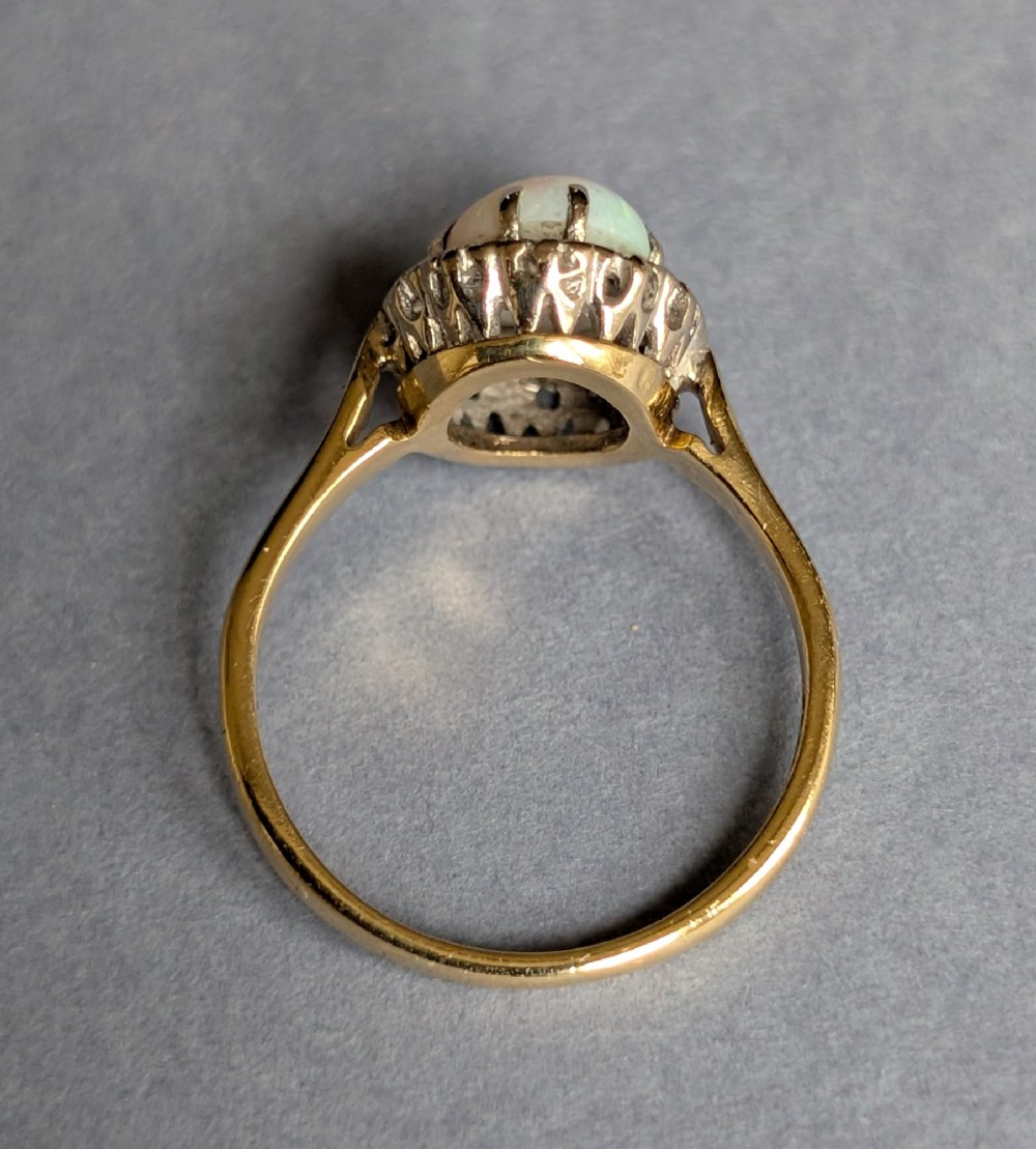 A mid-century 18ct gold ring featuring an oval cabochon opal framed by a halo cluster of small diamonds. View IX