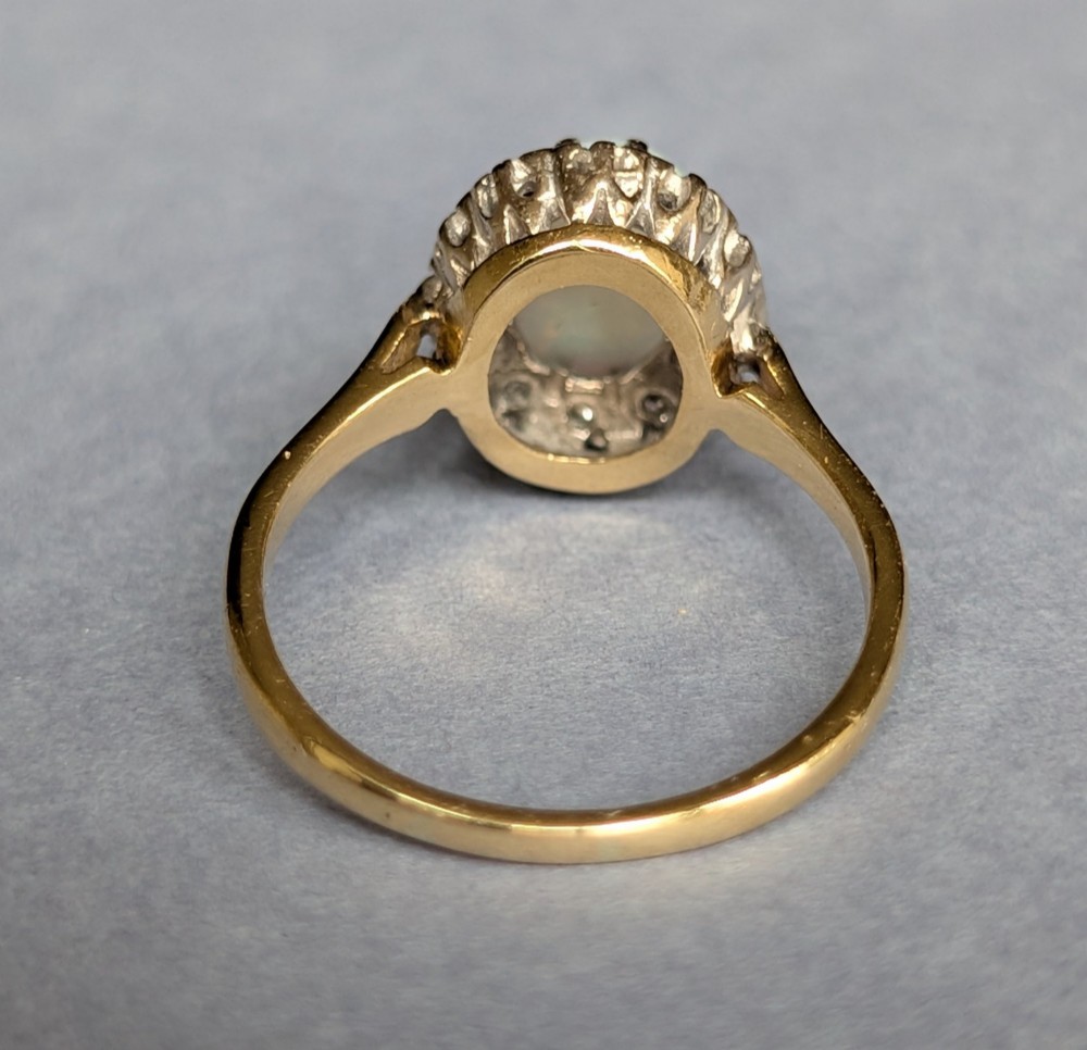 A mid-century 18ct gold ring featuring an oval cabochon opal framed by a halo cluster of small diamonds. View X