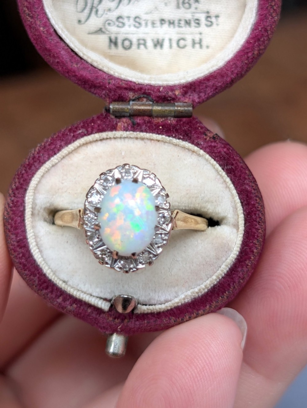 A mid-century 18ct gold ring featuring an oval cabochon opal framed by a halo cluster of small diamonds. View XI