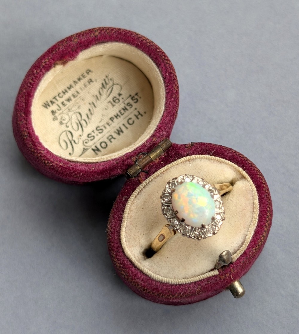 A mid-century 18ct gold ring featuring an oval cabochon opal framed by a halo cluster of small diamonds. View XII