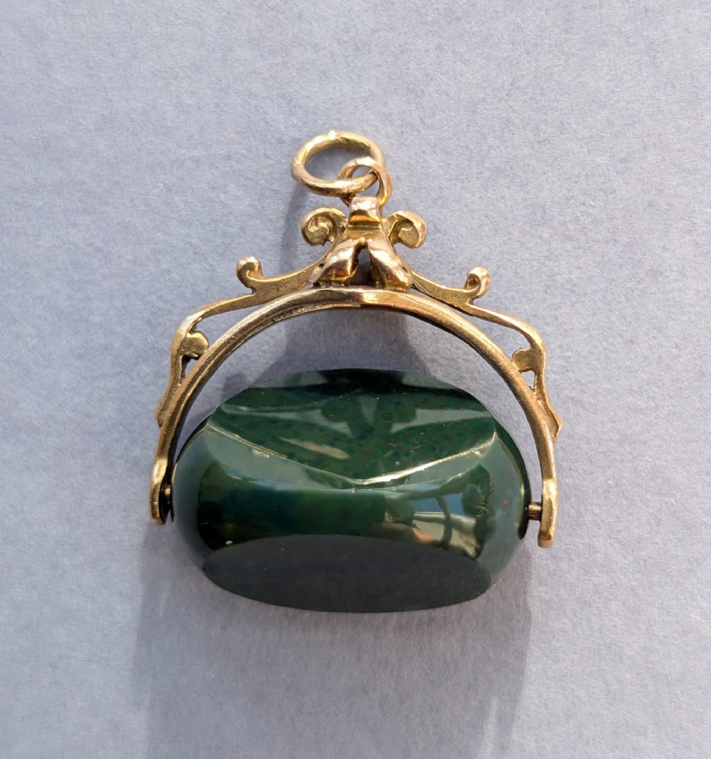 An antique 9ct gold spinning fob pendant featuring a polished dark green bloodstone within an ornate scrolled gold swivel frame.