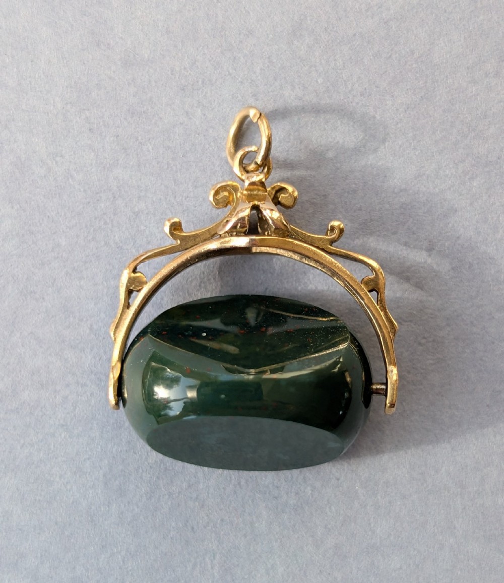 An antique 9ct gold spinning fob pendant featuring a polished dark green bloodstone within an ornate scrolled gold swivel frame. View II